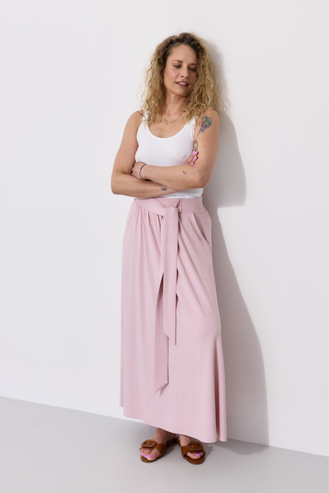 Różowa spódnica maxi z wiązaniem, biała koszulka i brązowe sandały – stylowy look na co dzień