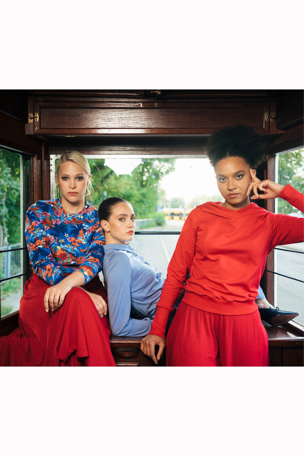 Trzy kobiety w stylowych, kolorowych ubraniach siedzą w tramwaju – moda polska, wygodna i elegancka