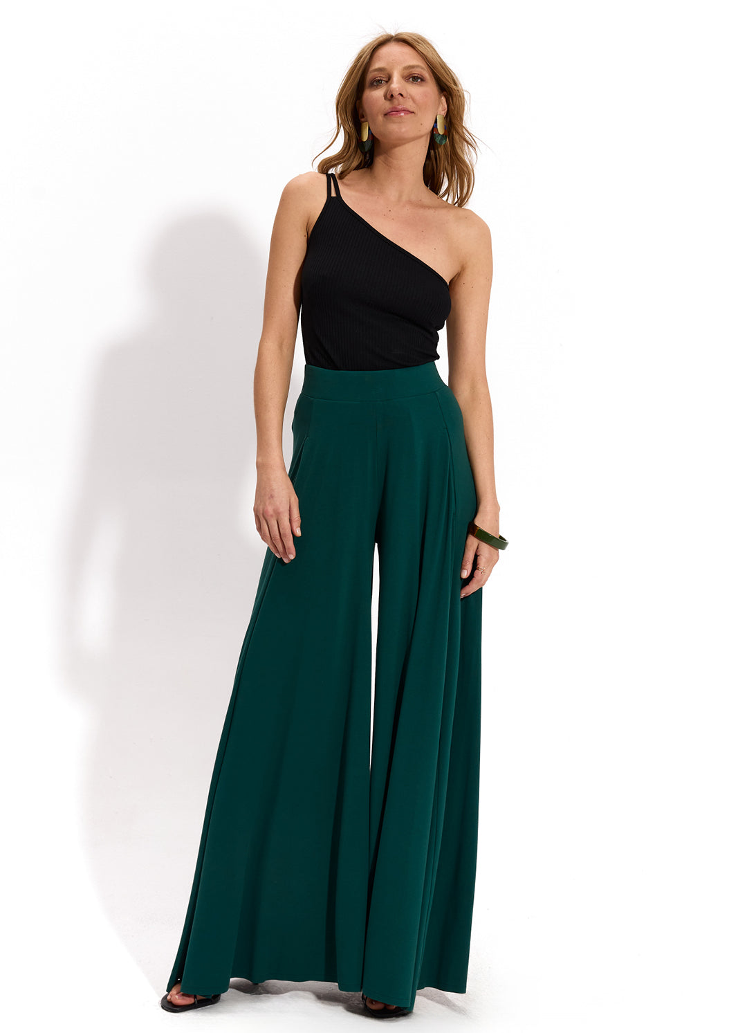 Kobieta w zielonych spodniach wide leg i czarnej bluzce jednoremieniowej, stylowa i wygodna moda