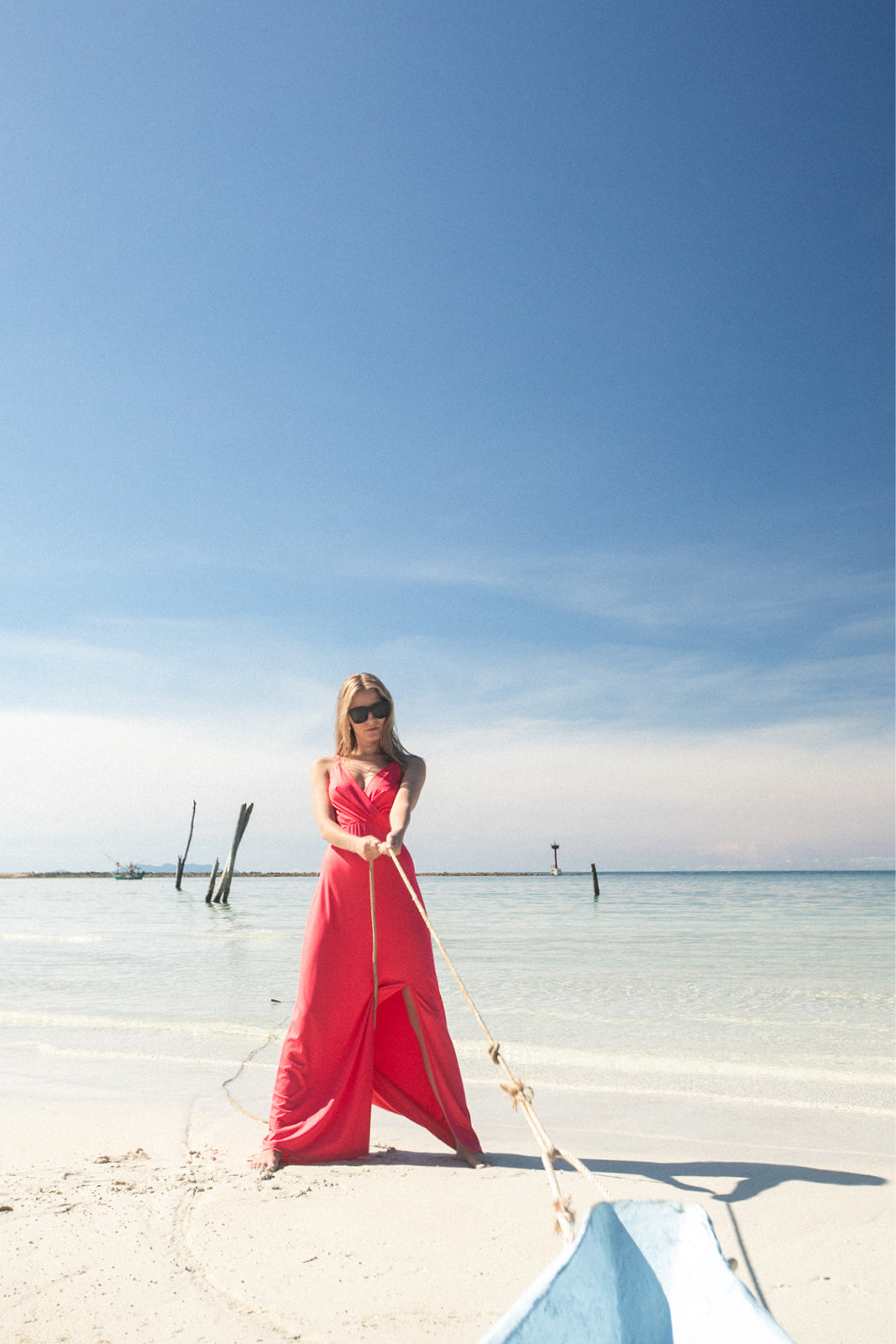 Kobieta w czerwonej sukience na plaży, trzymająca linę łodzi. Moda letnia, stylowa i wygodna.